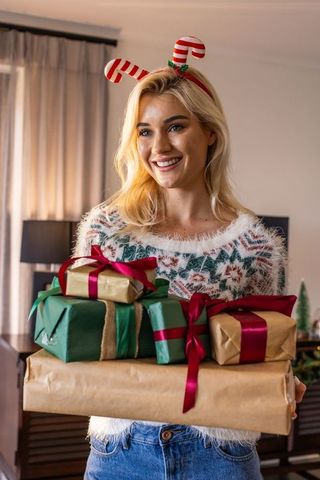 Smiling young woman holding christmas gifts wearing fuzzy sweater and candy cane headband
