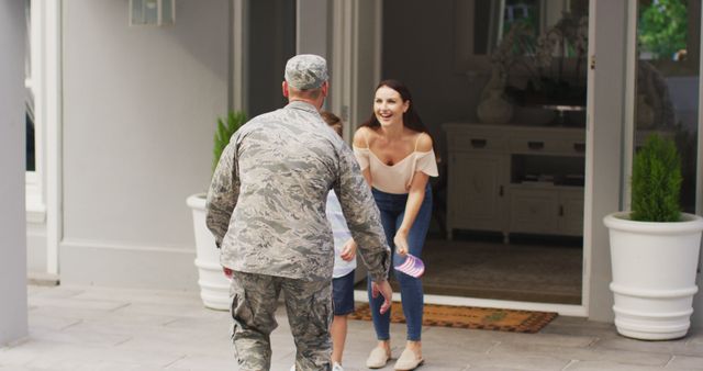 Happy caucasian male soldier lifting son and greeting wife outside their house. soldier returning home to family.