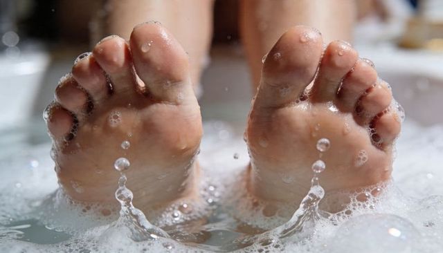 Relaxing bare feet floating in bubbly bathtub close-up with spa foam and droplets