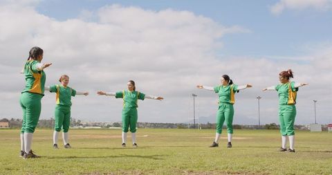 Female softball teammates warming up with arm stretches on field