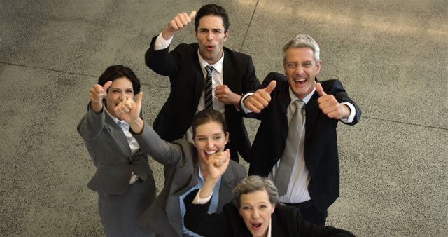 Diverse group of professionals in business attire are happily cheering and showing thumbs up, celebrating a goal or project completion. Use this image to depict teamwork, corporate success, motivation, and office celebrations.