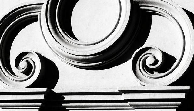 Ornate classical facade ornament with roundel and volute scrolls, high-contrast black-white