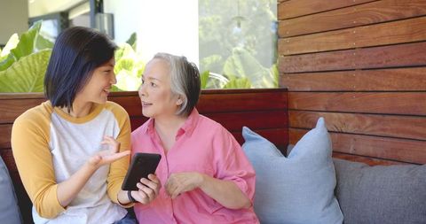 Mother and daughter discussing over smartphone on home couch
