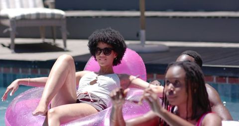 African american friends relaxing on pink inflatable pool float in sunny backyard summer