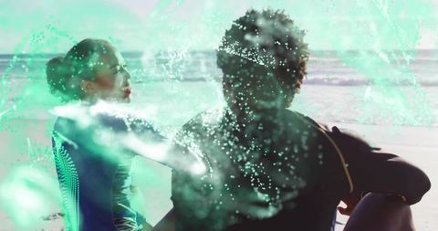 Sitting surfers sharing sunlit beach moment with teal particle overlay