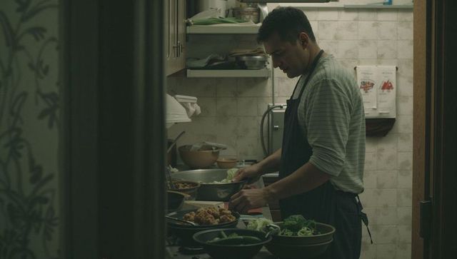 Chef plating bowls in narrow kitchen with moody lighting, focused mise en place and prep