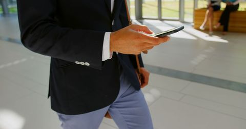 Businessman Walking in Office Lobby Using Mobile Phone