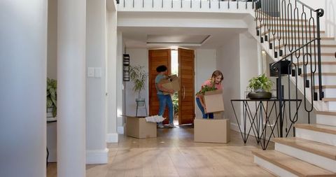 Couple Unpacking Boxes in New Home Foyer with Wooden Flooring and Modern Decor