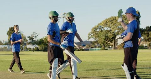Cricket players walking off pitch in blue jerseys during sunny park match
