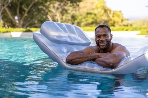 Mature man reclining on inflatable pool lounger, smiling, sunny backyard summer relaxation