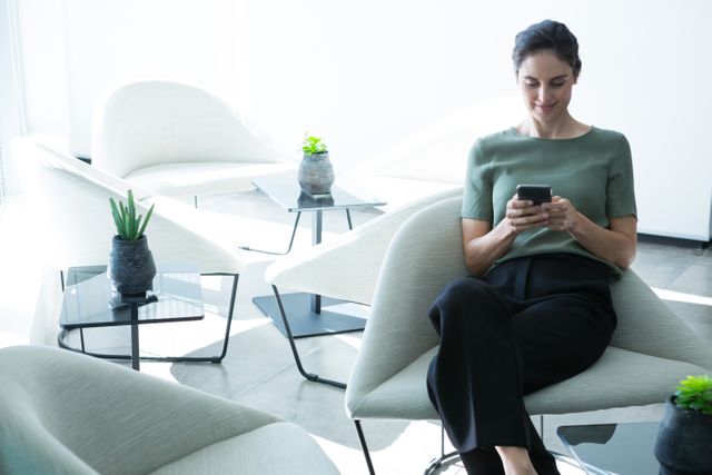 Female executive using mobile phone on chair in office