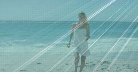 Sunlit woman walking along shoreline in white sundress and sunglasses with teal rays
