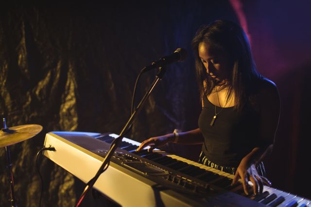 Female musician playing piano on stage in a dimly lit nightclub. Ideal for use in articles about live music, nightlife, entertainment, and musical performances. Suitable for promoting concerts, music events, and showcasing talented artists.