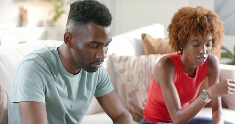 African-American couple sitting on couch having tense conversation at home