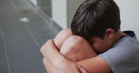 Lonely Boy Sitting In Hallway Holding His Knees Thoughtfully