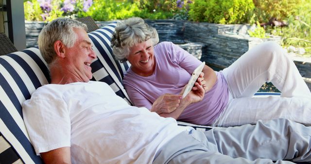 A senior Caucasian couple enjoys a relaxing moment together, laughing while looking at a tablet, with copy space. Their joyful interaction highlights the comfort and happiness of retirement life.