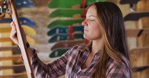Young Female Skateboarder Choosing Skateboard in Skate Shop