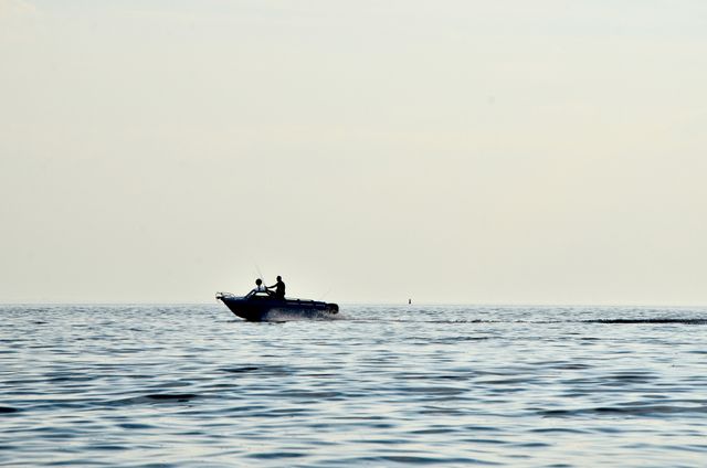 Man fishing alone on motorboat in open sea during daylight. Perfect for themes around recreation, adventure, tranquility, and nature. Useful in articles or websites related to fishing, boating, travel, and relaxation.