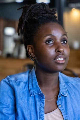Thoughtful african woman gazing upward in coffeehouse portrait wearing denim shirt