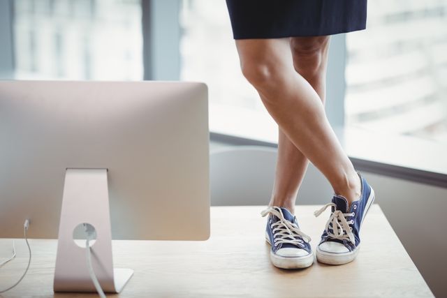 Low section of woman in canvas shoes standing on office table