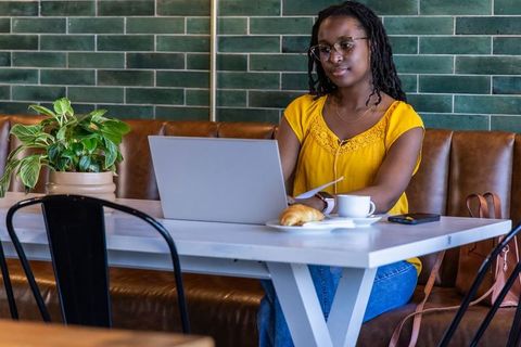 Remote worker in cafe working on laptop with coffee and pastry, casual modern productivity