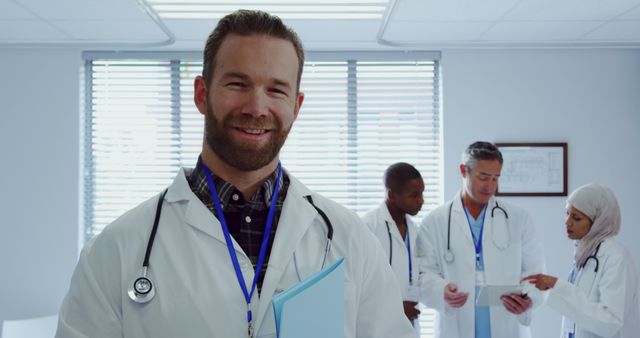 Smiling Doctor Holding Folder with Colleagues in Background - Download Free Stock Images Pikwizard.com