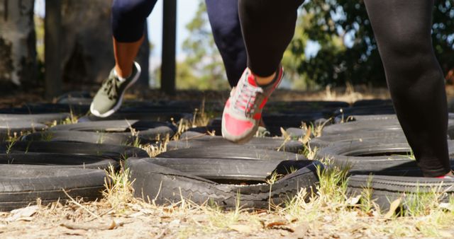 Image shows participants running through a tire obstacle course during an outdoor fitness session. They are using agility and coordination, focusing on improving their endurance and physical strength. This image could be used to illustrate themes related to fitness programs, athletic training, outdoor team building activities, and wellness promotions.