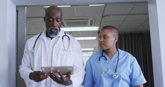 African american male doctor and female health worker discussing over digital tablet at hospital. healthcare and medical concept