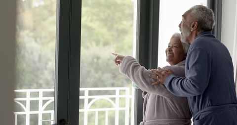 Senior Couple in Morning Robes Looking Out Window