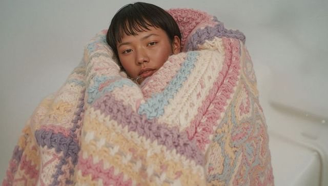 Cozy portrait of woman wrapping in pastel crochet blanket in bathtub