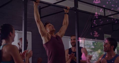 Group cheering while man performing pull-up on gym rig during strength training with pink overlay