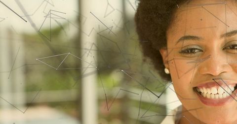 Smiling woman leaning by patterned glass showing pearl earring and white collar, daylight closeup