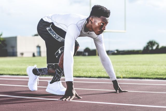 Male athlete in starting position on running track, focusing on sprint. Wearing sportswear and showing determination. Ideal for use in fitness motivation, sports training, competitive racing, athletic advertisements, and outdoor activities promotions.