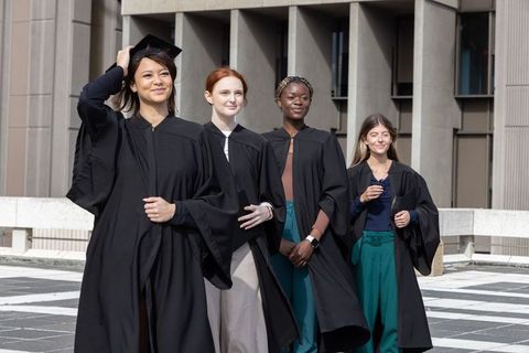 Diverse female graduates celebrating on campus terrace wearing black gowns and mortarboards