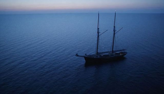 Two-masted schooner drifting at twilight over calm sea with pastel horizon and ample copy space