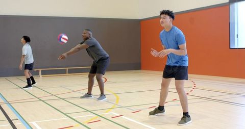 Diverse male teammates practicing indoor volleyball receiving and passing on gym court