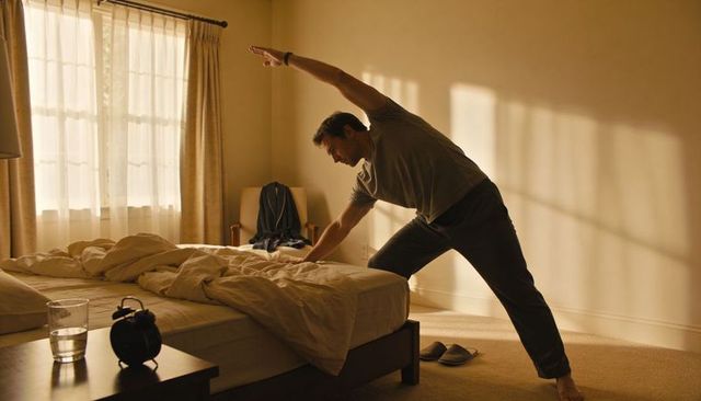 Man stretching and reaching over unmade bed during sunlit morning routine in cozy bedroom