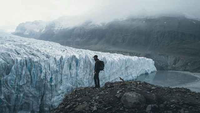 Standing hiker surveying towering blue glacier and glacial lake on rugged moraine