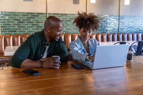 African american coworkers collaborating over laptop in modern coffee shop