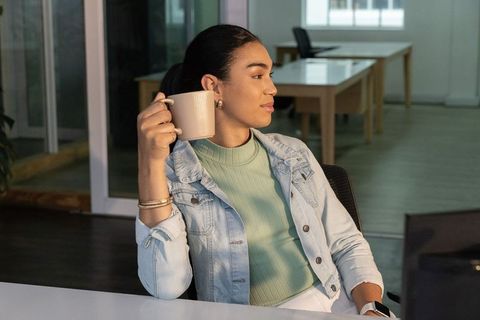 Young professional enjoying coffee at modern open-plan office desk, relaxed work break