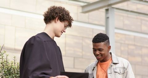 Graduate celebrating with friend while viewing diploma outside modern campus building