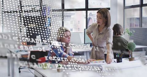 Women collaborating on design and code review in modern open office with laptop and monitors