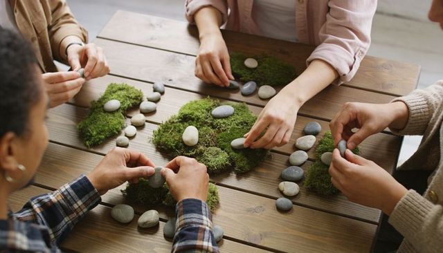 Hands arranging moss and pebbles on wooden table for group nature craft workshop