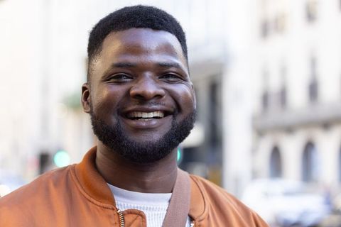 Confident african man smiling on urban street wearing orange jacket and crossbody bag