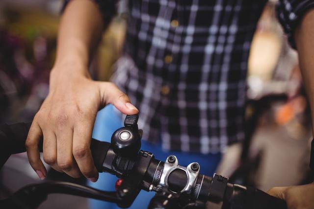 Close-up view of mechanic ringing bicycle bell in workshop. Ideal for use in articles on bike maintenance, cycling safety, mechanical work, and transportation topics. Suitable for websites and blogs focusing on biking, repair shops, and DIY repair tutorials.