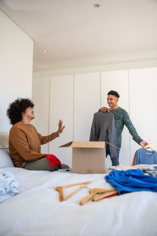 Diverse friends organizing clothes in bedroom, collaboration and teamwork
