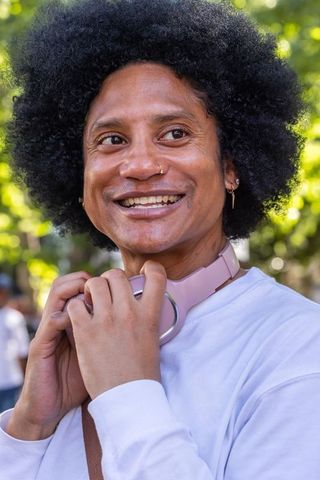 African american man smiling holding pink headphones in sunlit park portrait