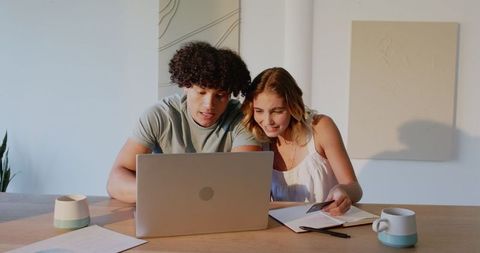 Young Couple Smiling at Laptop in Sunlit Home Workspace