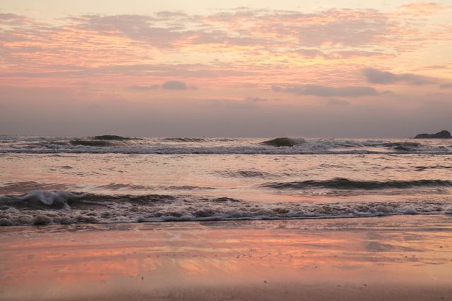 Image capturing the serene beauty of sunrise with gentle waves near a sandy beach. Ideal for backgrounds, travel brochures, meditation visuals, websites promoting coastal retreats or relaxation themes, and social media posts about nature and tranquility.