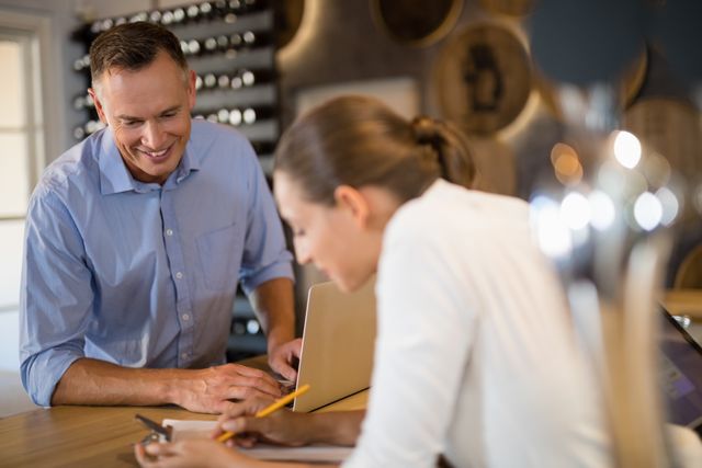 Smiling manager and bartender discussing over clipboard in bar